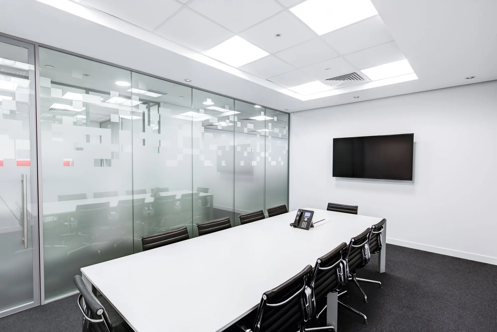 An empty boardroom with a long white table, black chairs and a frosted glass partition