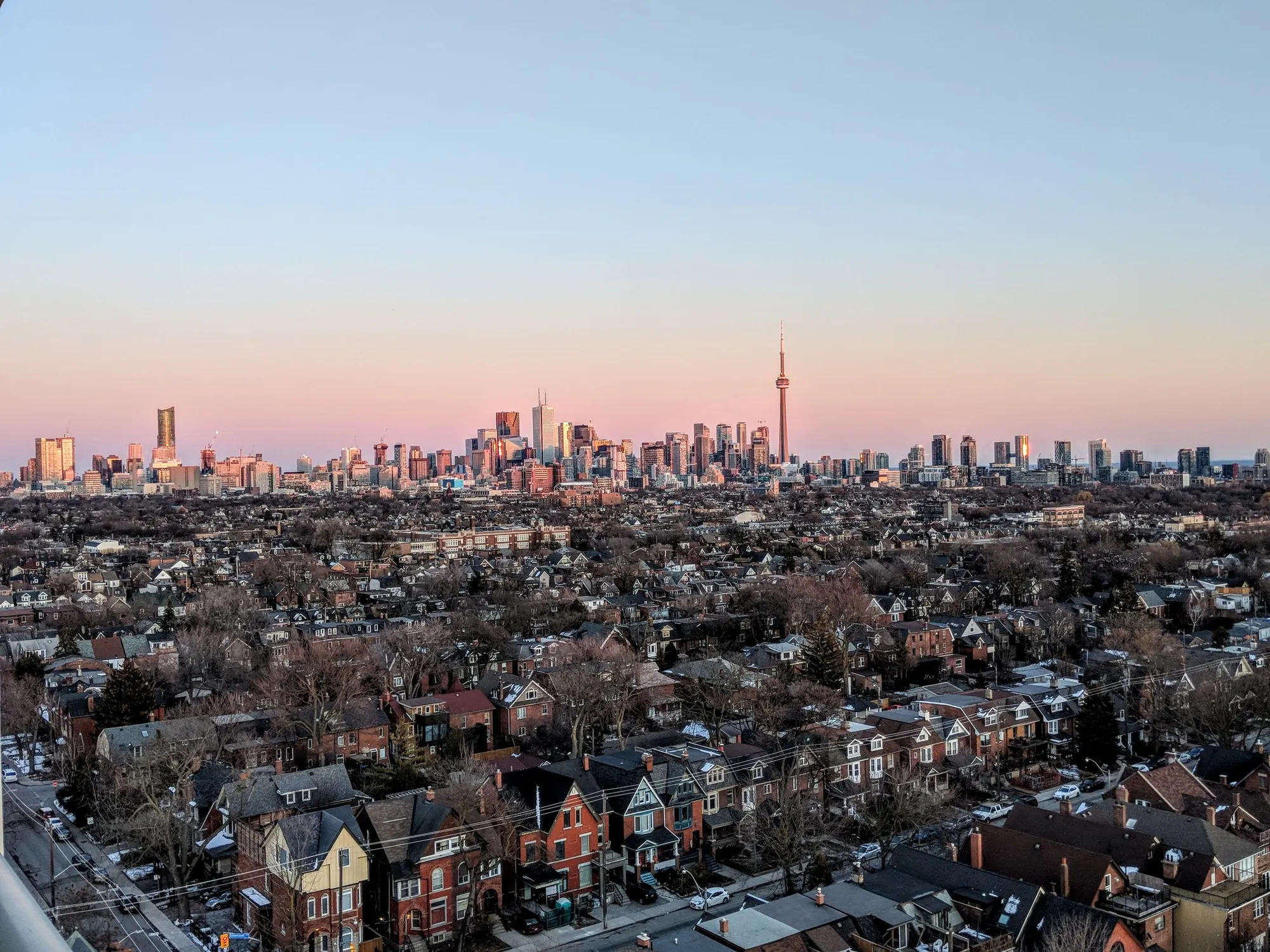 Toronto’s brick rooftops running toward the downtown skyline and the CN Tower at sunset