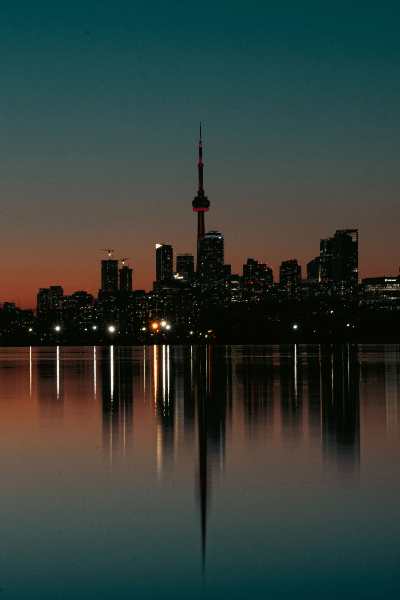 The Toronto skyline in silhouette at last light with the CN Tower lit above the water