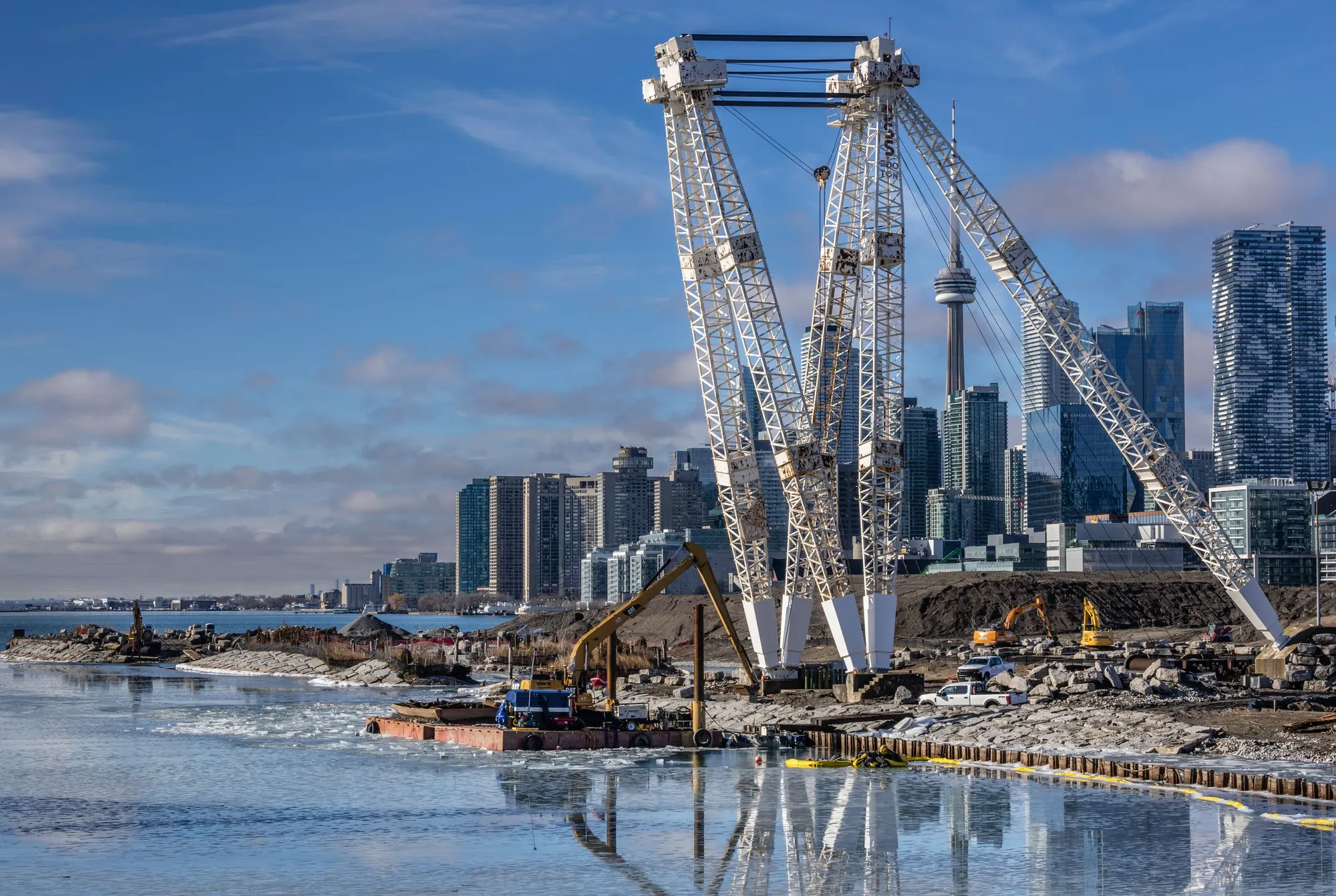 A lattice tower crane over a Toronto waterfront construction site with the CN Tower behind